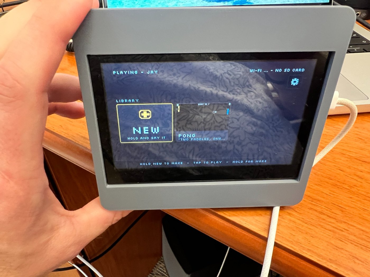 A small gray case holding a screen that shows a game library with a card labeled New and a card labeled Pong